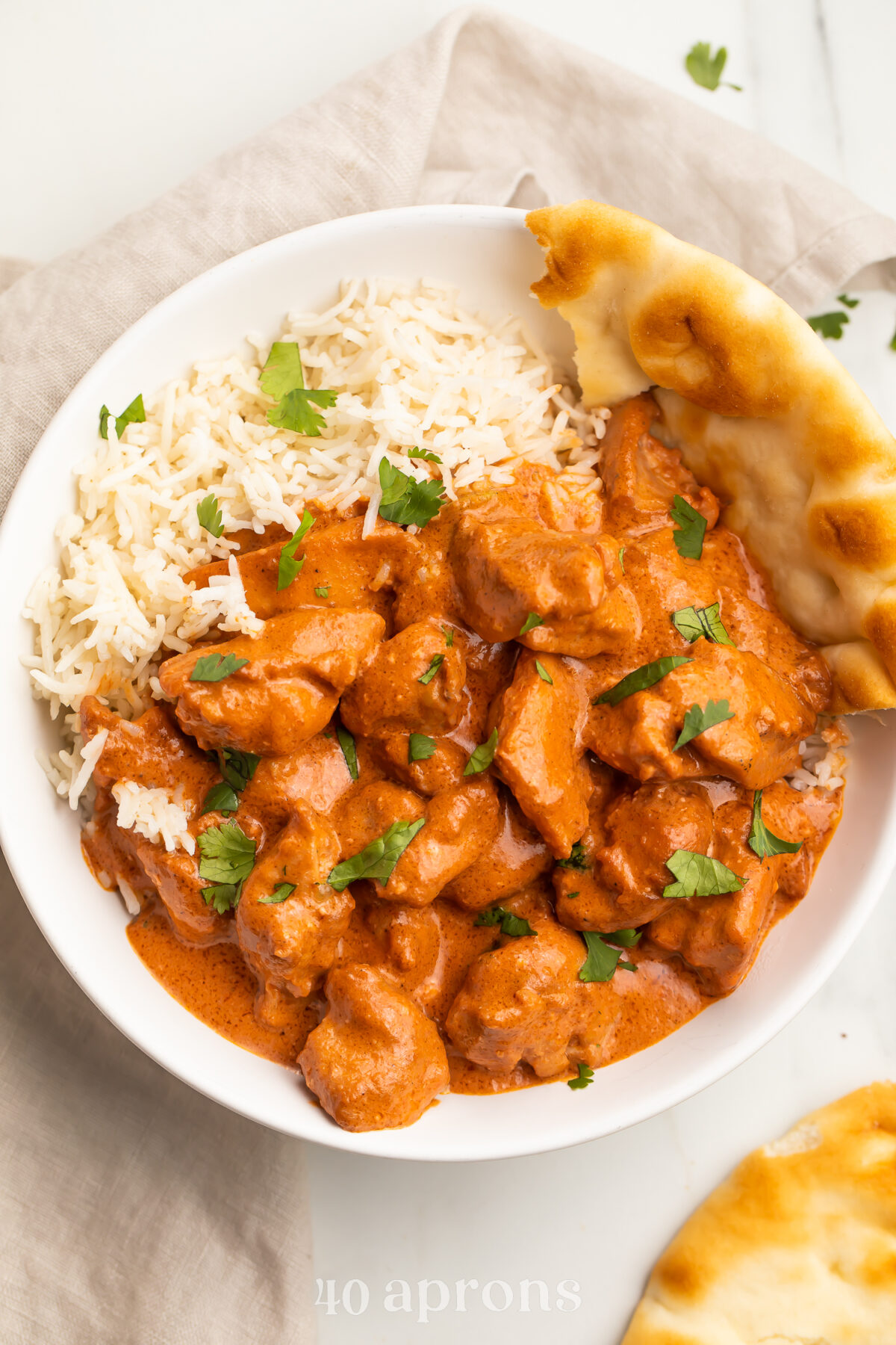 Zoomed out photo of butter chicken in a creamy red-orange sauce plated next to white rice and naan.