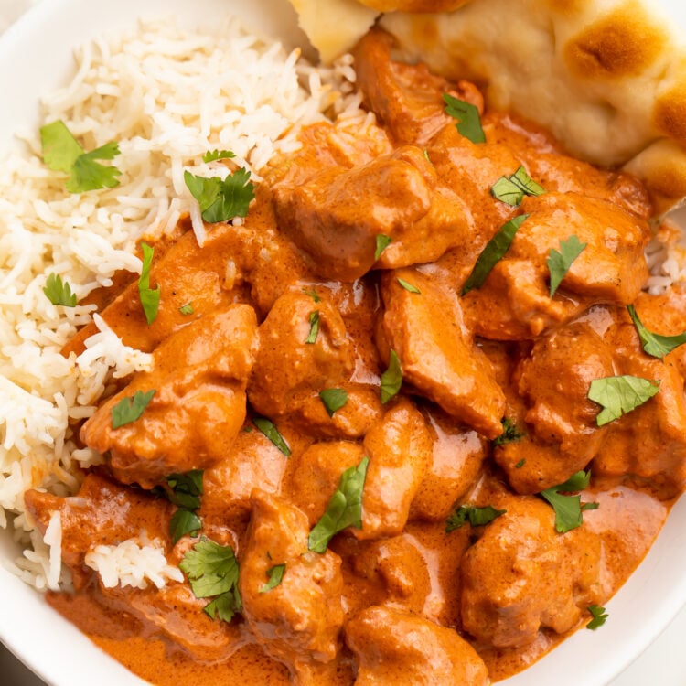 Overhead photo of butter chicken in a creamy red-orange sauce plated next to white rice and naan.