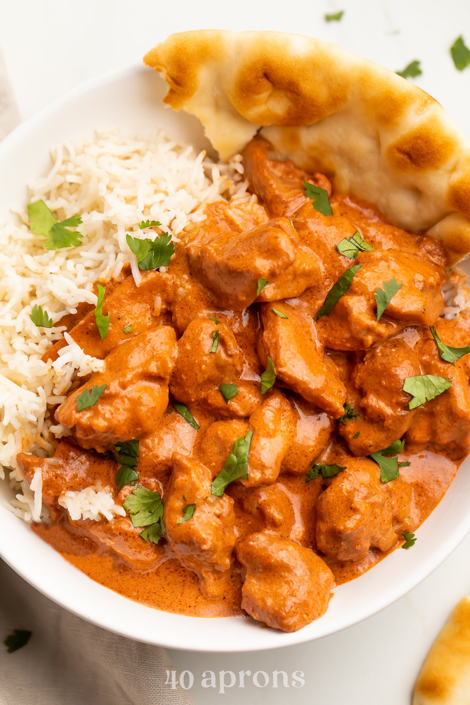 Overhead photo of butter chicken in a creamy red-orange sauce plated next to white rice and naan.