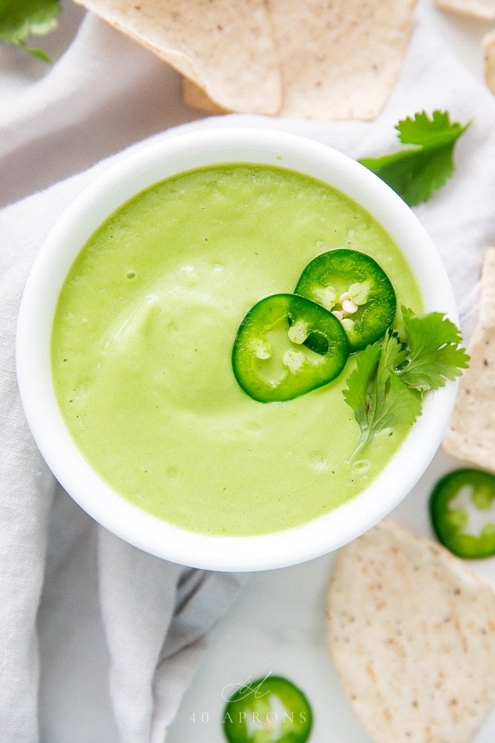 Bowl of pale green avocado dip garnished with fresh jalapeño rings and cilantro leaves