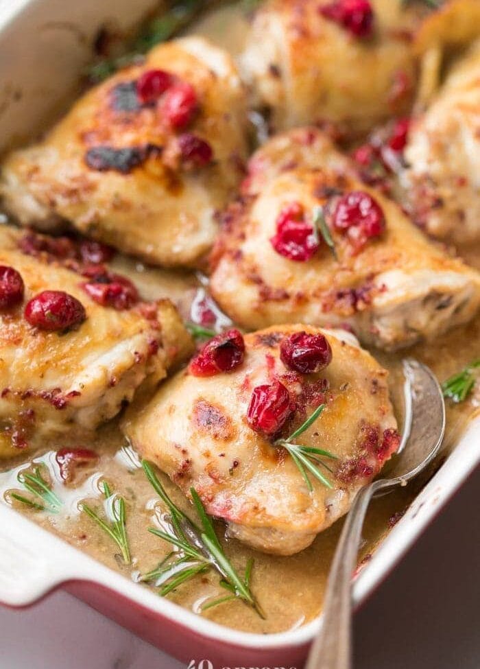 Paleo cranberry rosemary one pan chicken thighs in a baking dish with vintage spoon topped with cranberries and fresh rosemary