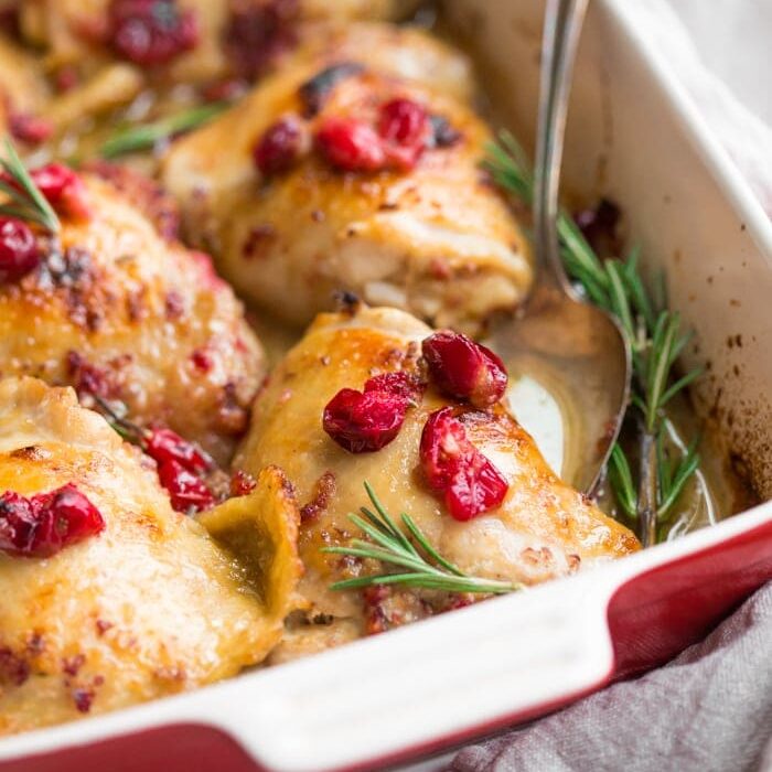 Paleo cranberry rosemary one pan chicken thighs in a baking dish topped with cranberries and fresh rosemary