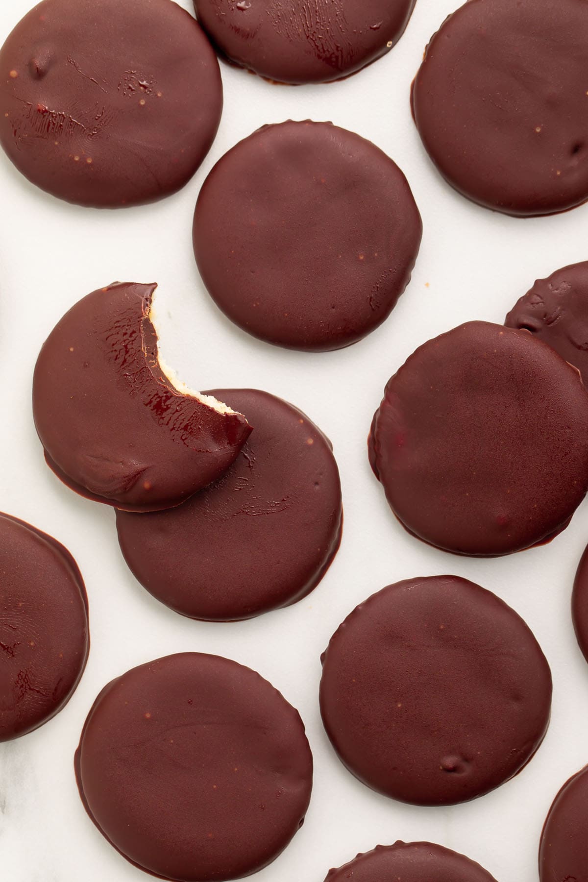 Vegan thin mints scattered across a countertop. A bite is missing from the topmost cookie.