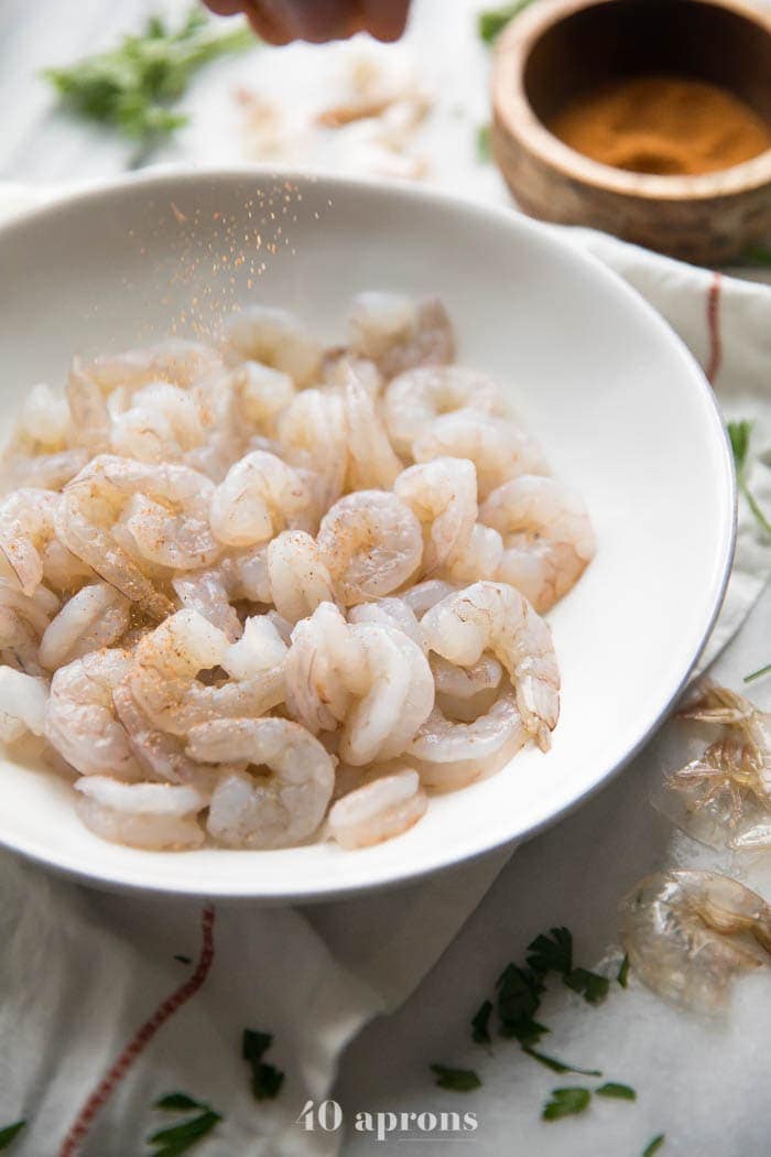 Shrimp in a bowl with Cajun seasoning being sprinkled over