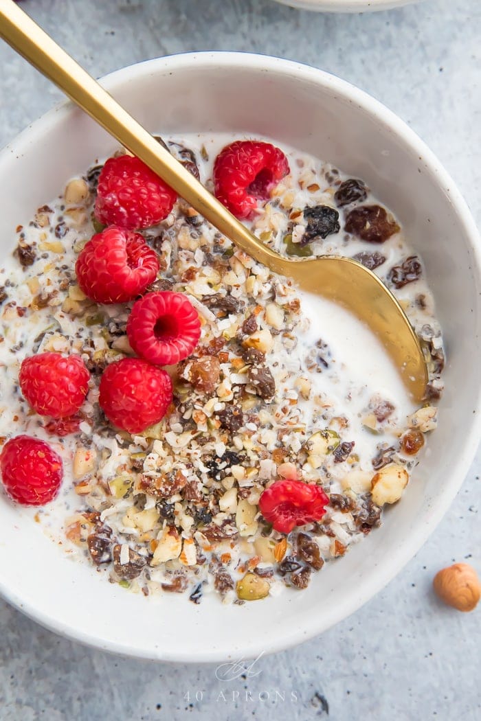 A bowl of paleo cereal with a gold spoon and raspberries on top