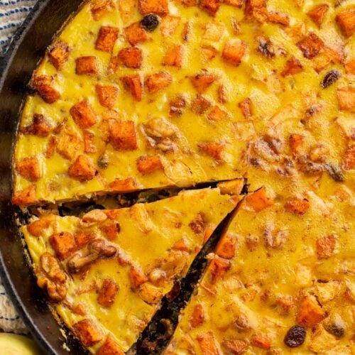 A large cast iron skillet holding a paleo breakfast bake. A wedge of the bake has been sliced already.