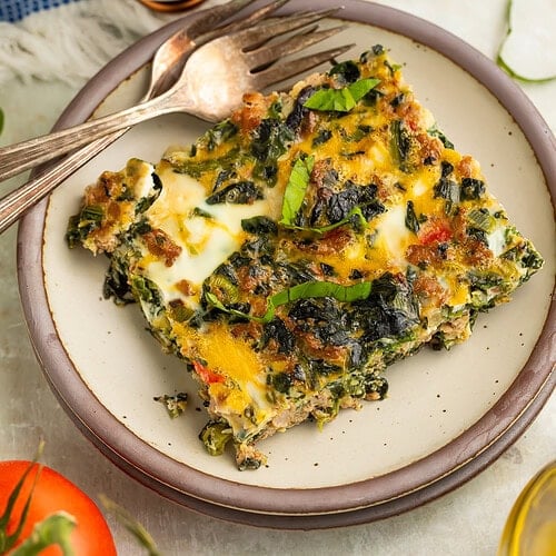 Slice of Whole30 breakfast bake with sausage, eggs, spinach, and bell peppers on a cream plate with a fork