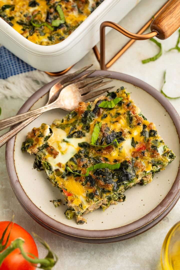 Slice of Whole30 breakfast bake with sausage, eggs, spinach, and bell peppers on a cream plate with a fork