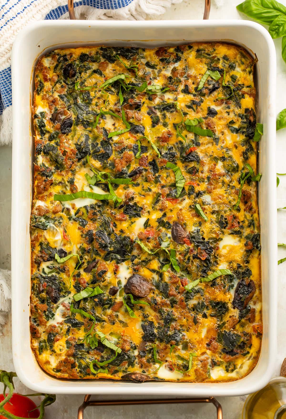Whole30 breakfast casserole with sausage, eggs, mushrooms, and spinach in a white baking dish, garnished with fresh basil.