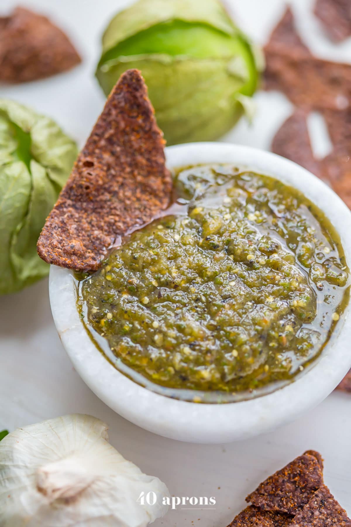 A bowl of green roasted salsa verde with a blue corn tortilla chip resting in the salsa.