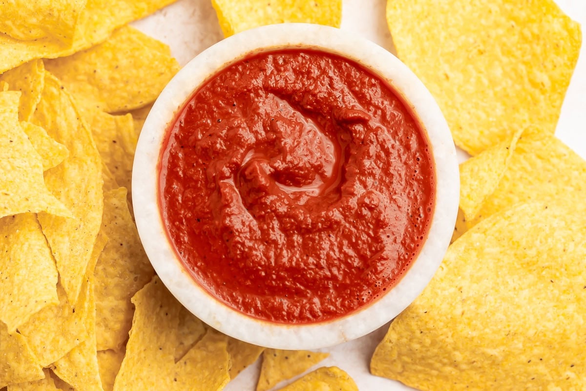 Rich, vibrantly red smoky guajillo salsa in a small bowl surrounded by tortilla chips.