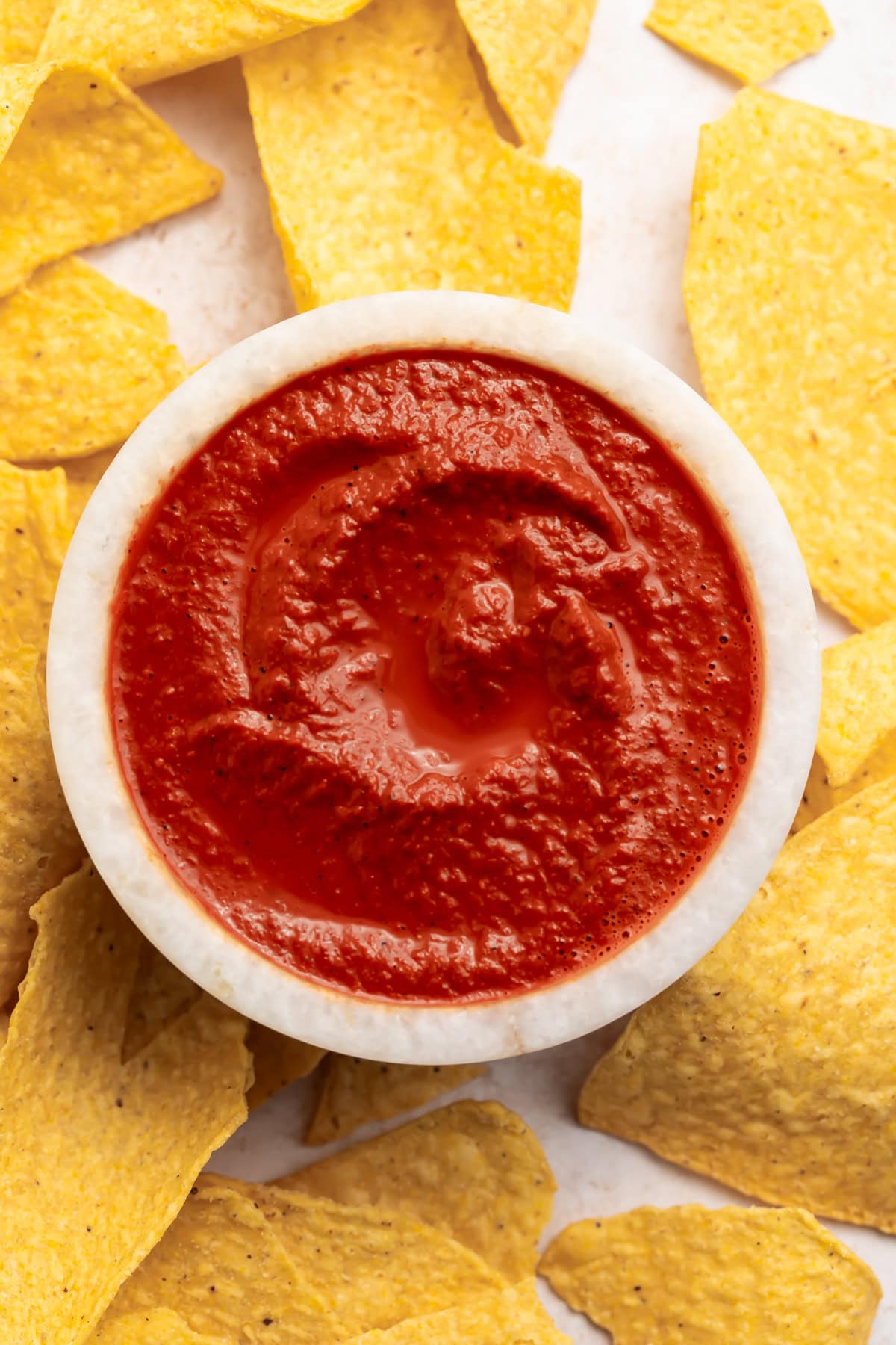 Rich, vibrantly red smoky guajillo salsa in a small bowl surrounded by tortilla chips.