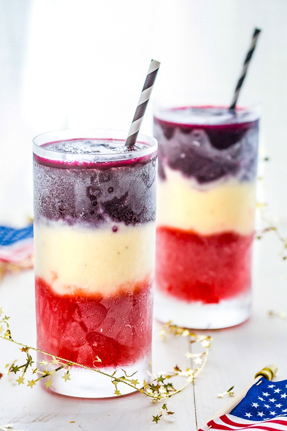 Two tall glasses containing red, white, and blue layered cocktails.