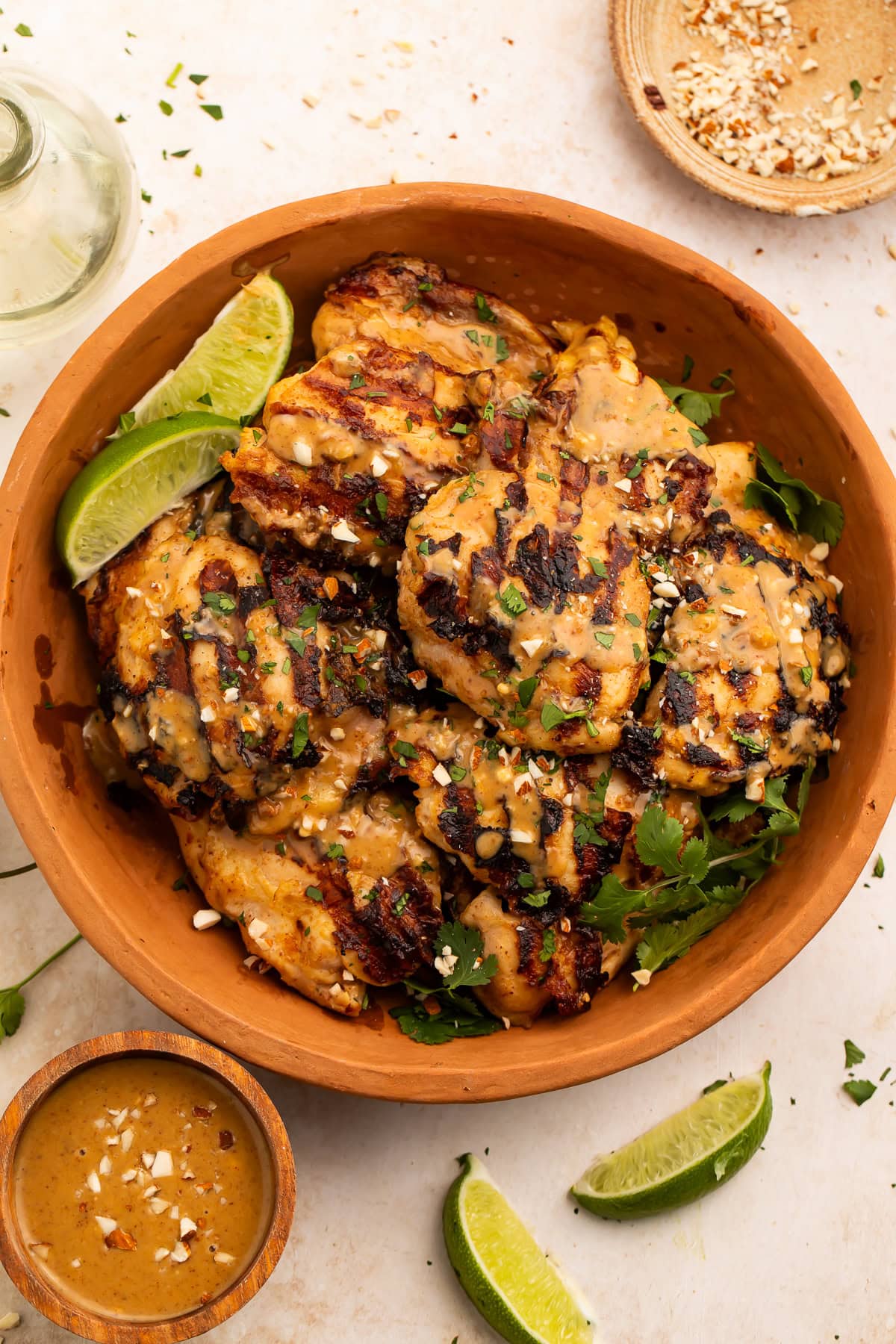 Overhead view of peanut-free chicken satay in a terracotta bowl with dipping sauce and lime