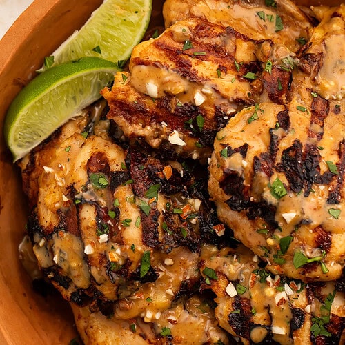 Grilled peanut-free chicken satay in a terracotta bowl with almond sauce, cilantro, and lime wedges