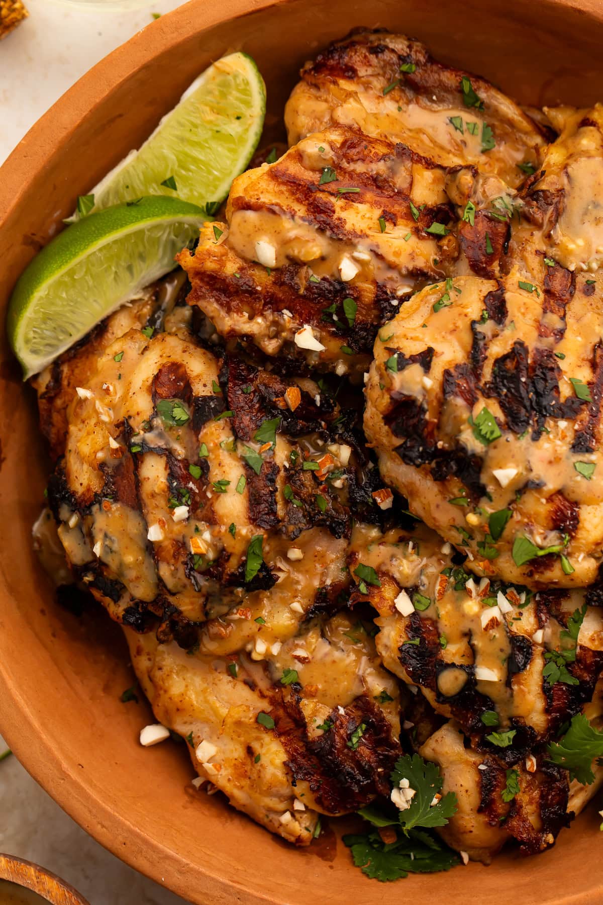 Grilled peanut-free chicken satay in a terracotta bowl with almond sauce, cilantro, and lime wedges