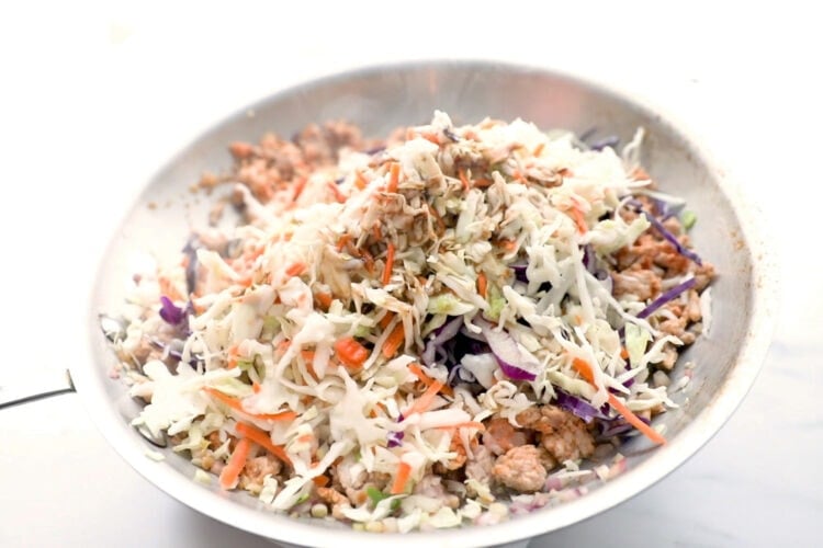 Coleslaw mix added to a large skillet with ground pork.