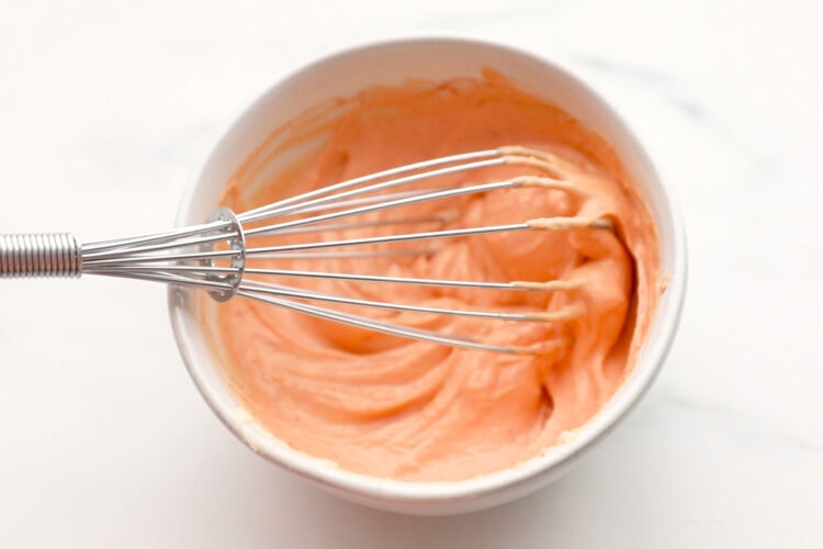 Creamy chili sauce in a mixing bowl with a whisk.