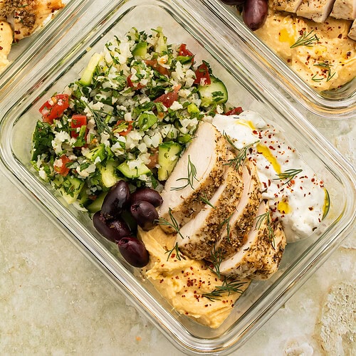 Close up of glass meal prep containers with chicken, cauliflower rice and yogurt sauce.