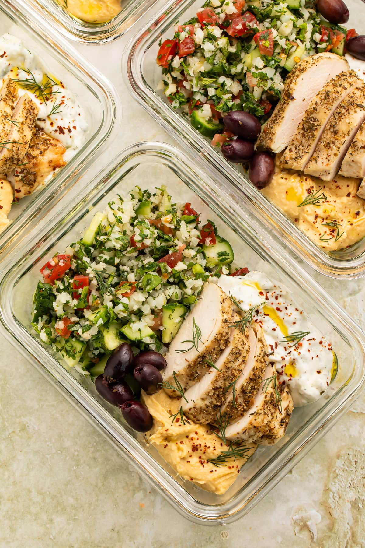 Close up of glass meal prep containers with chicken, cauliflower rice and yogurt sauce.