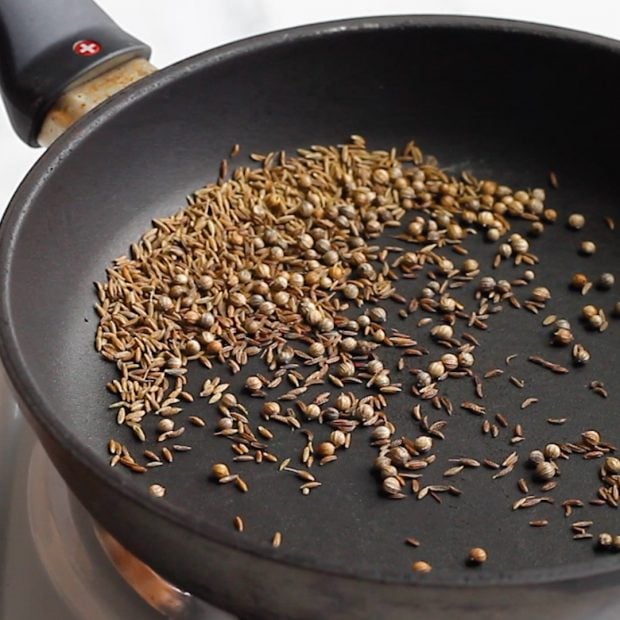 whole spices being toasted in a black skillet