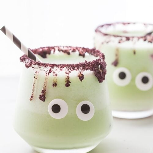 These "monsteritas" are healthy Halloween margaritas spiked with cucumber and jalapeño for a trick and treat all in one! Sweetened with honey, these healthy Halloween margaritas are super festive and fun without any refined sugar or artificial coloring. With a freeze-dried blueberry rim and two candy eyes, these healthy Halloween margaritas are a must make for any adult Halloween party!