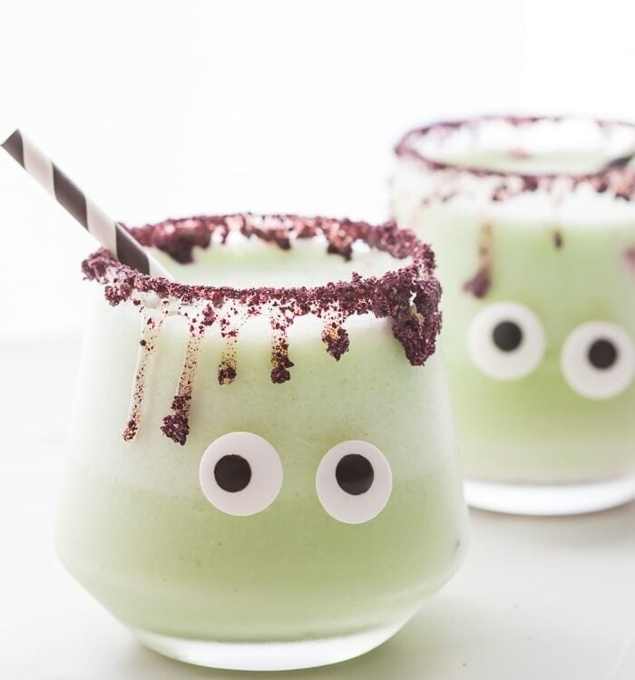 These "monsteritas" are healthy Halloween margaritas spiked with cucumber and jalapeño for a trick and treat all in one! Sweetened with honey, these healthy Halloween margaritas are super festive and fun without any refined sugar or artificial coloring. With a freeze-dried blueberry rim and two candy eyes, these healthy Halloween margaritas are a must make for any adult Halloween party!