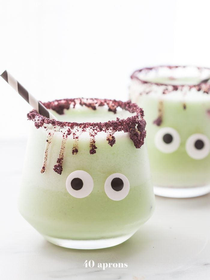 Monsteritas green Halloween cocktails with purple dripping rim and candy monster eyes in glasses with a black and white straw