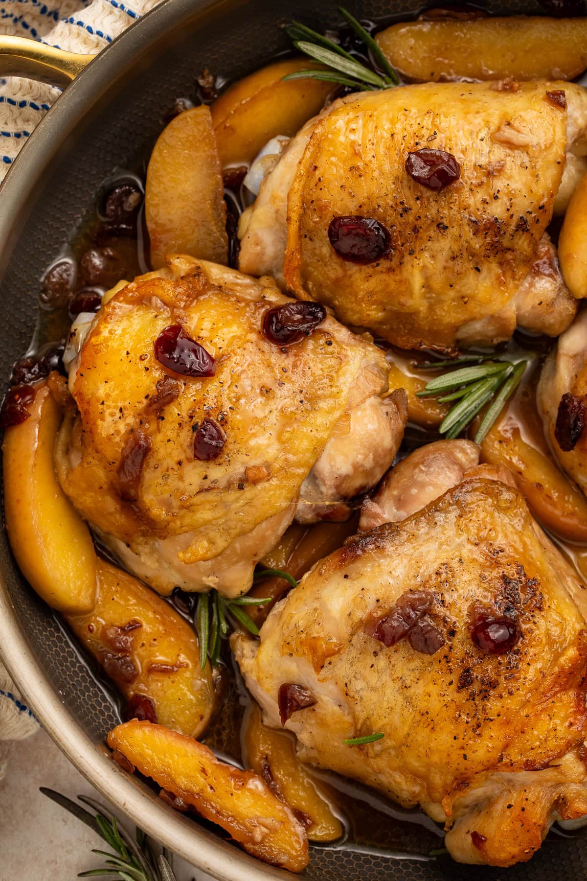 Paleo chicken thighs with caramelized apples, cranberries, and rosemary in glossy pan sauce.