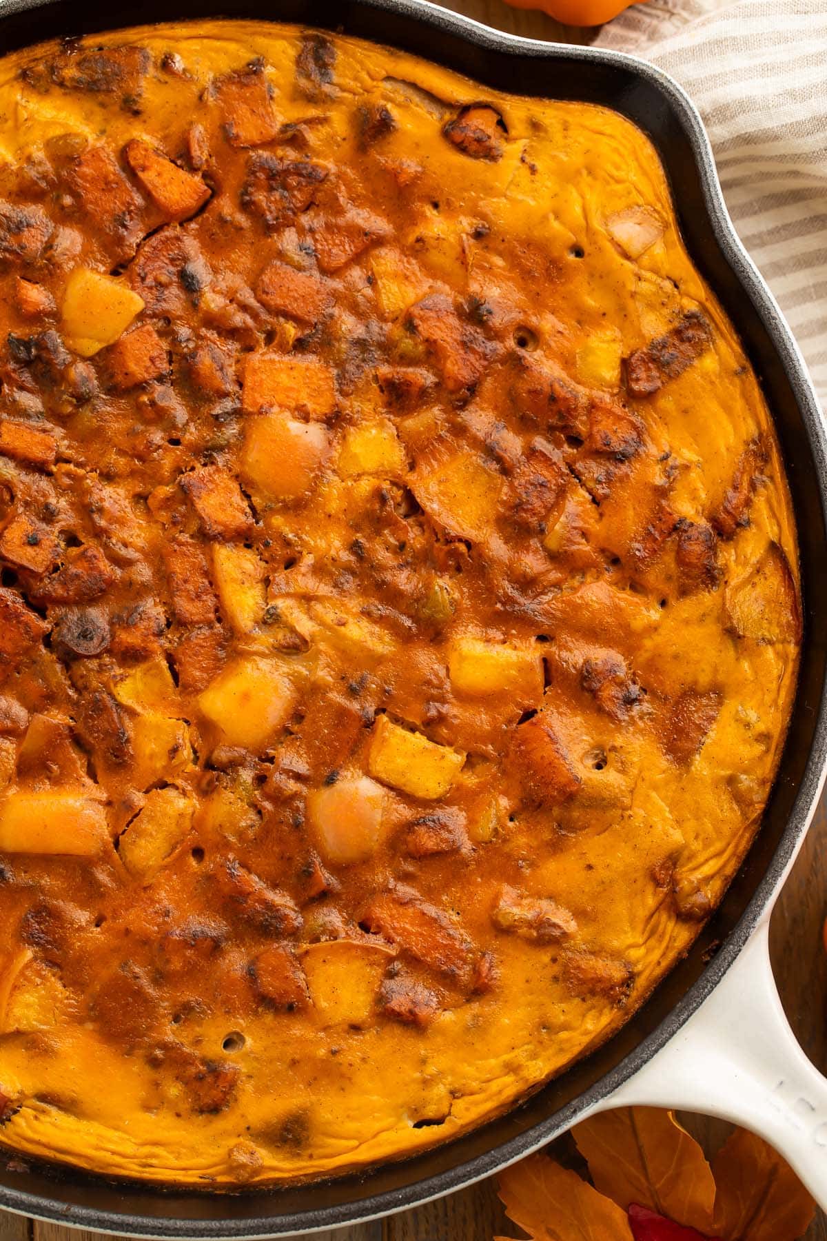 A large cast-iron skillet holding a fully-baked paleo pumpkin breakfast bake, loaded with sweet potatoes, apples, walnuts, and eggs.