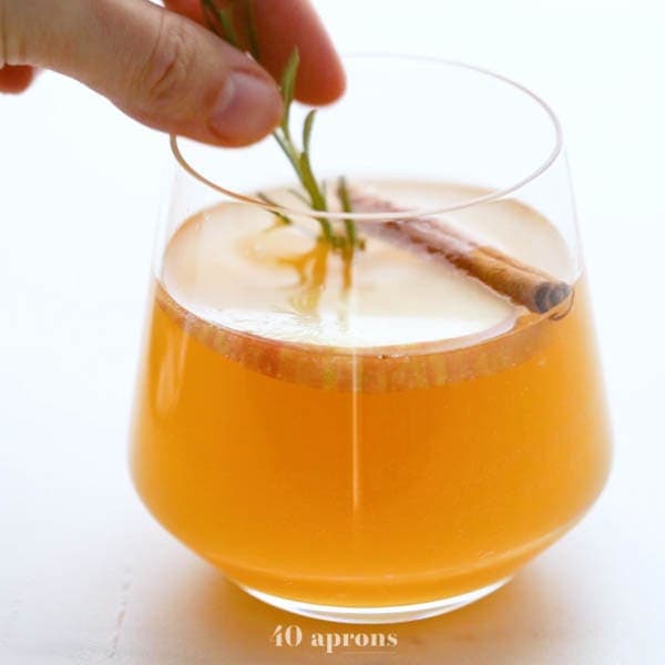 Cinnamon apple cider mimosa in a cup with an apple slice, cinnamon stick and rosemary