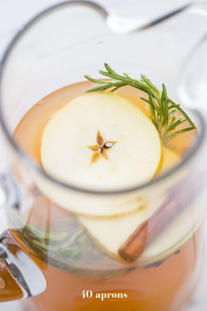 Slice of apple, rosemary, and cinnamon stick in a jug of apple cider mimosa