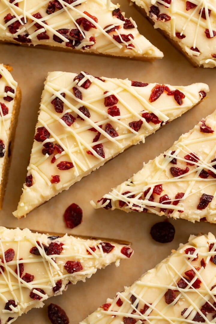 Triangular cranberry bliss bars topped with cranberries and cream cheese frosting.