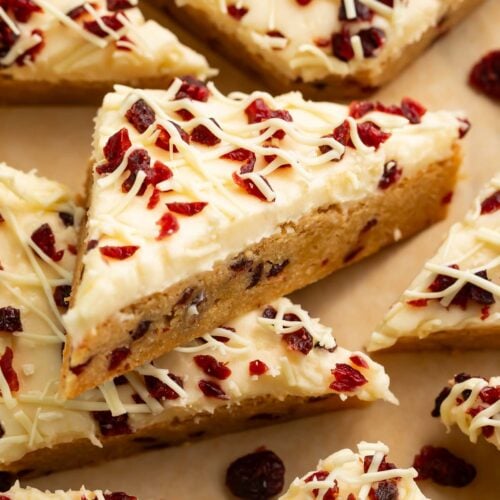 Triangular cranberry bliss bars topped with cranberries and cream cheese frosting.