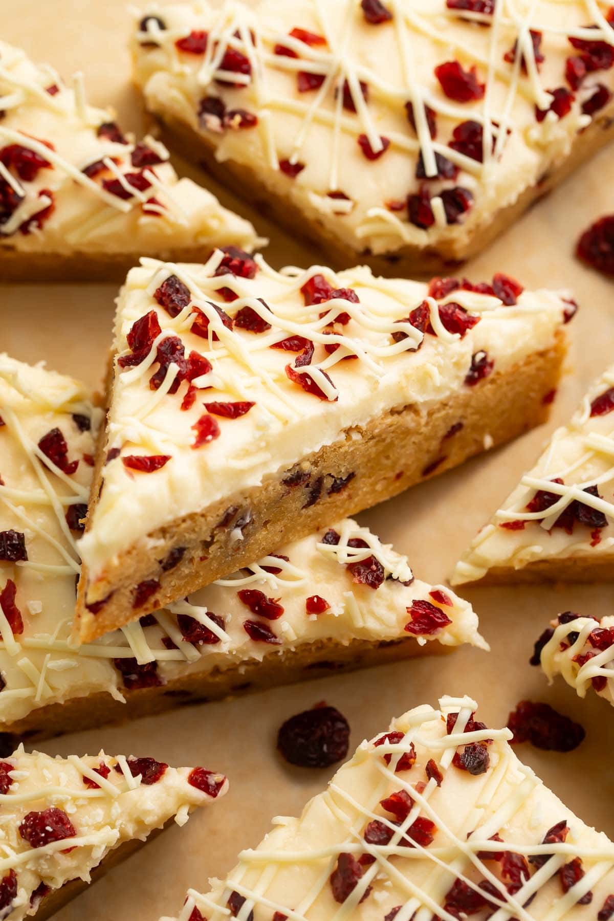 Triangular cranberry bliss bars topped with cranberries and cream cheese frosting.