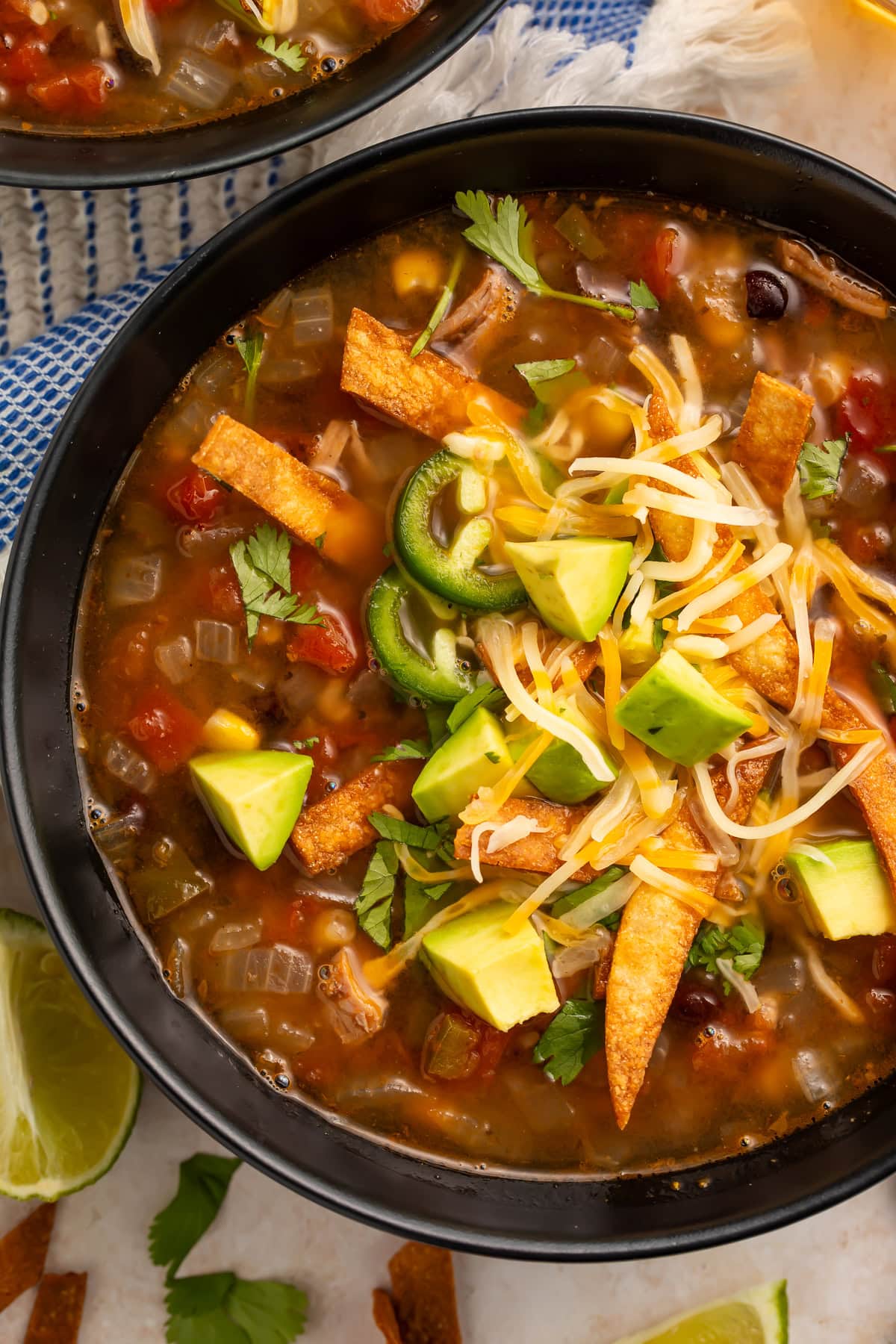 Bowl of leftover turkey tortilla soup topped with avocado, shredded cheese, jalapeño slices, crispy tortilla strips, and fresh cilantro
