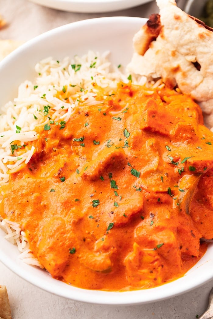 A bowl of chicken tikka masala over basmati rice with a slice of naan