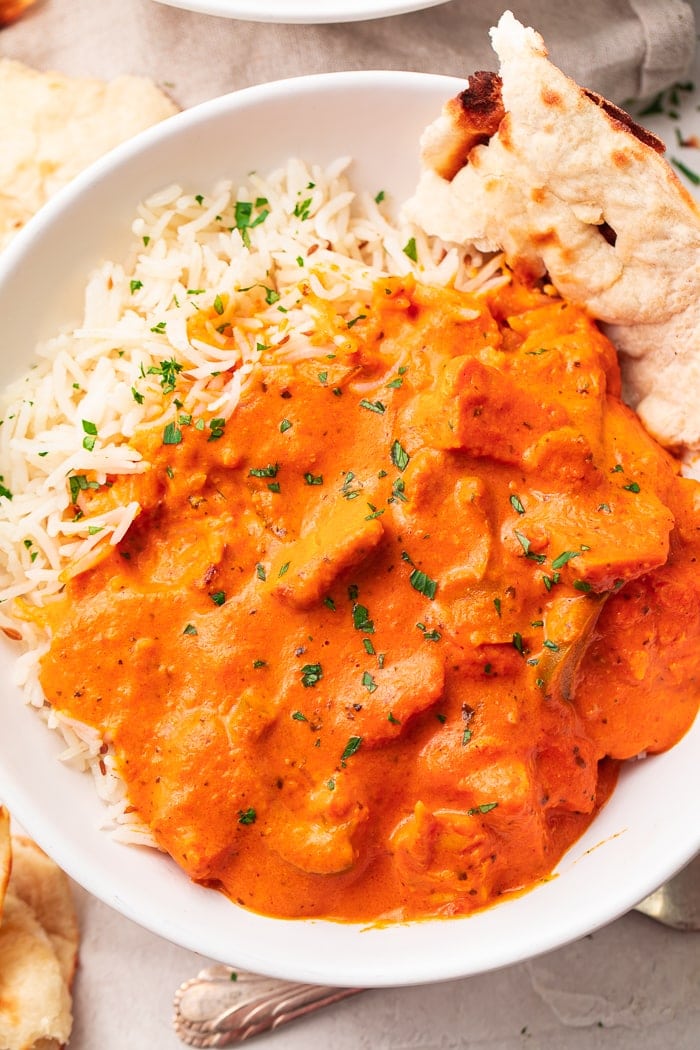 A bowl of chicken tikka masala over basmati rice with a slice of naan
