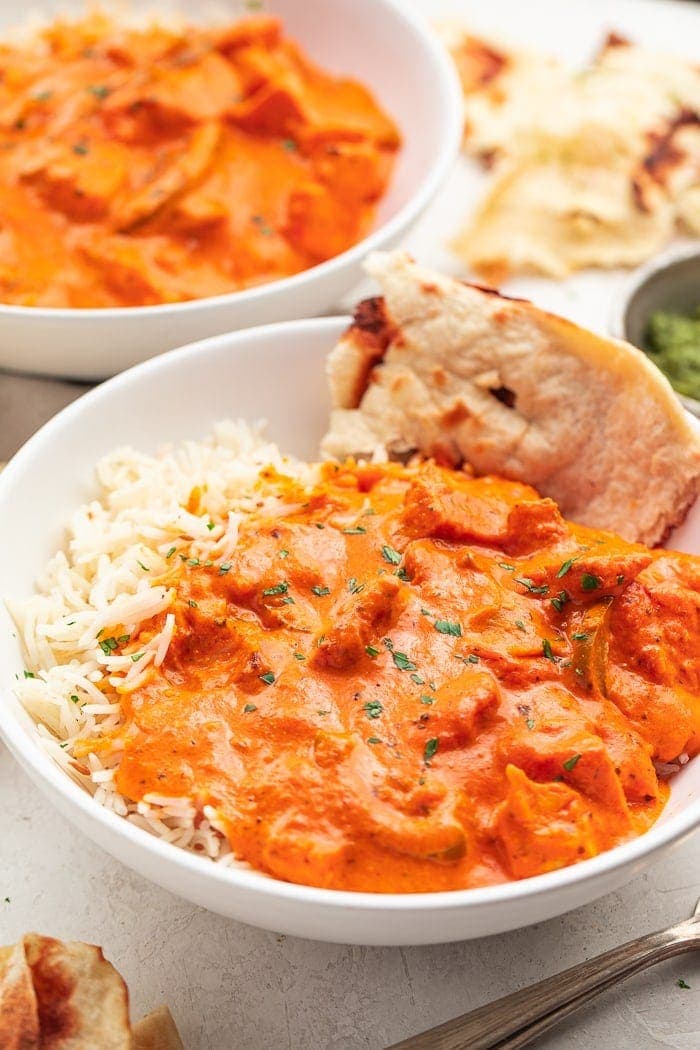 A bowl of chicken tikka masala over basmati rice with a slice of naan