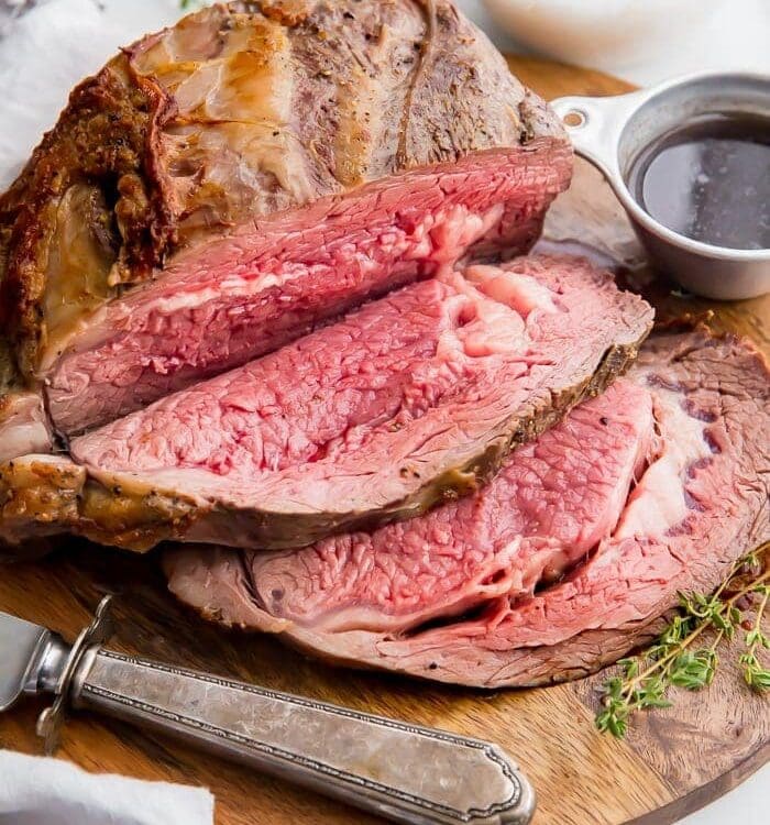 Medium rare prime rib sliced on a board with au jus in a cup