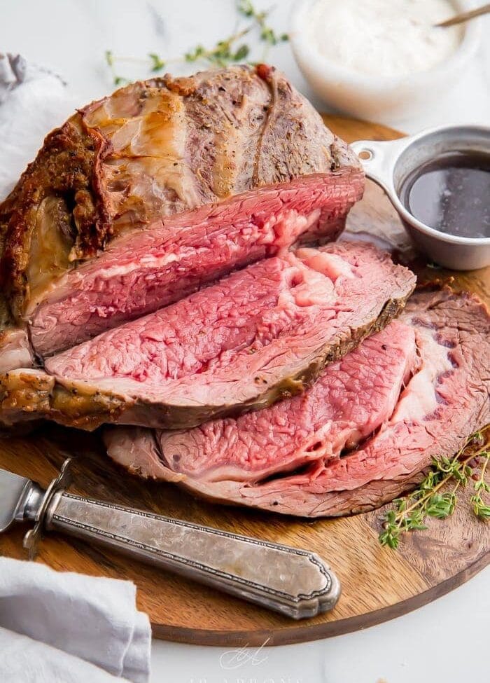 Medium rare prime rib sliced on a board with au jus in a cup