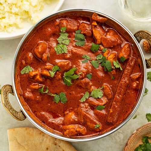 Metal dish of dairy free butter chicken surrounded by sundries.