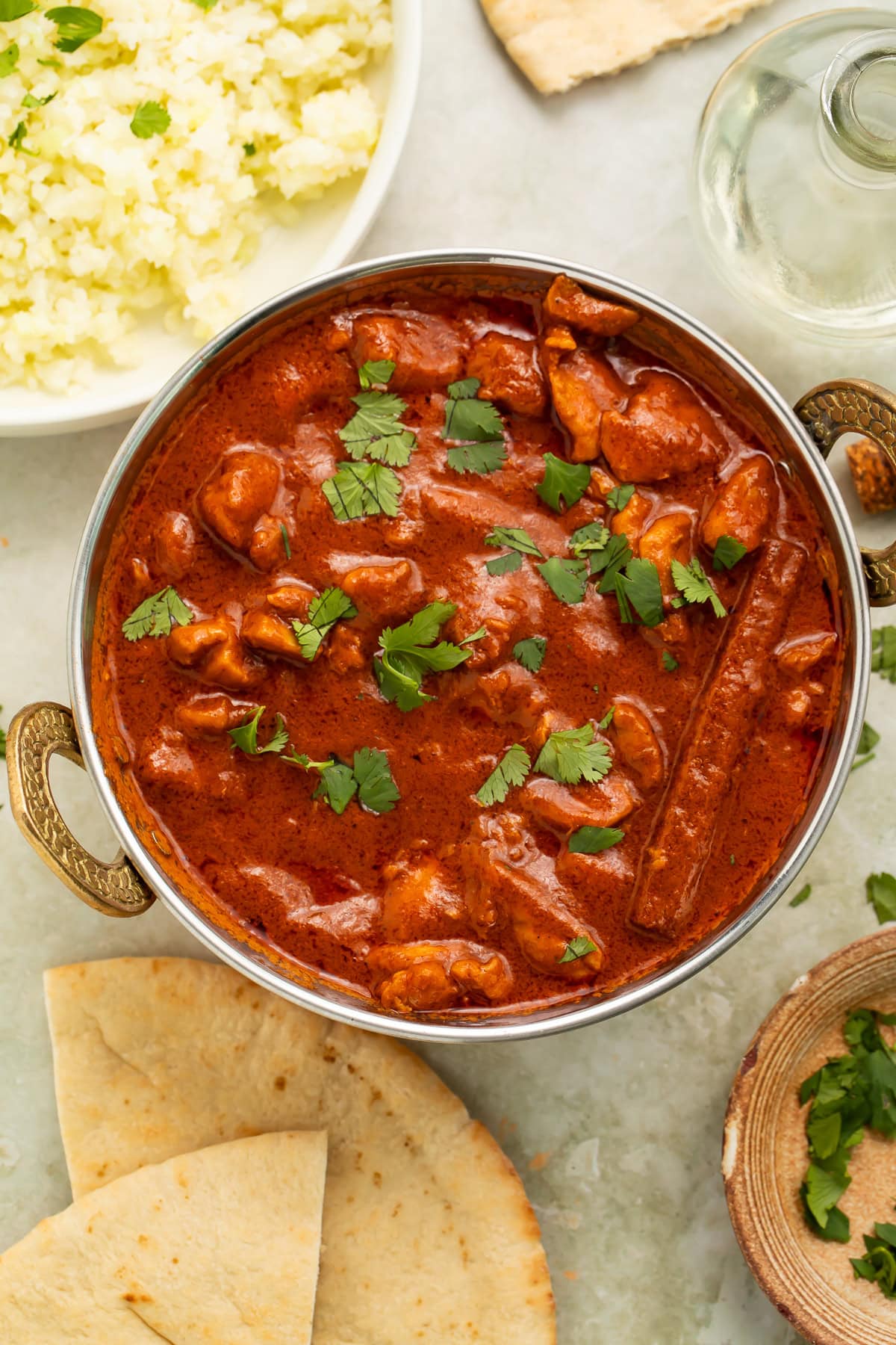 Metal dish of dairy free butter chicken surrounded by sundries.