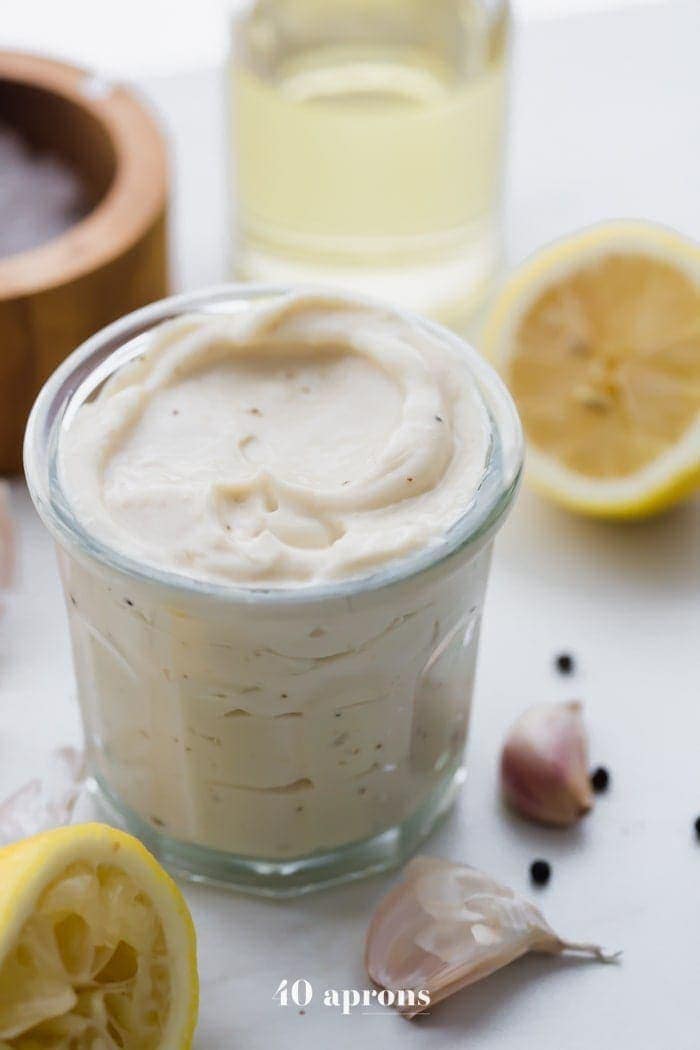 Whole30 Caesar dressing in a jar with lemons, garlic, peppercorns, and light tasting olive oil in a bottle