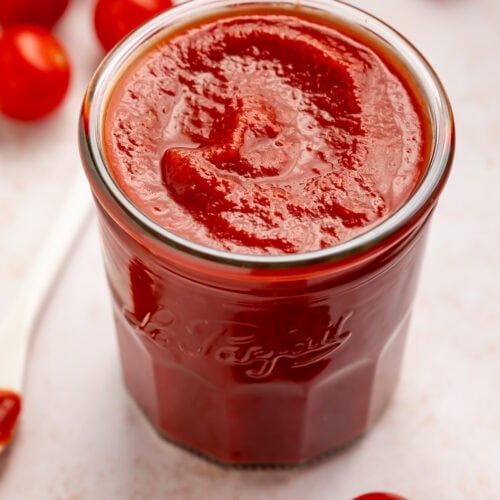 Jar of homemade tomato ketchup with cherry tomatoes scattered around.