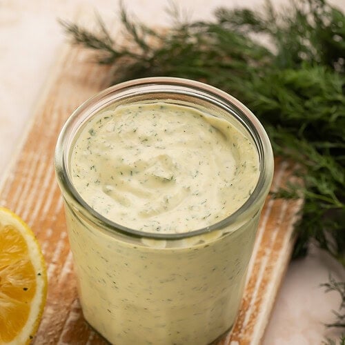 Creamy Whole30 ranch dressing in a glass jar on a wooden board with lemon and garlic