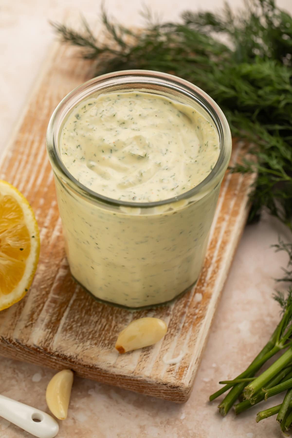 Creamy Whole30 ranch dressing in a glass jar on a wooden board with lemon and garlic