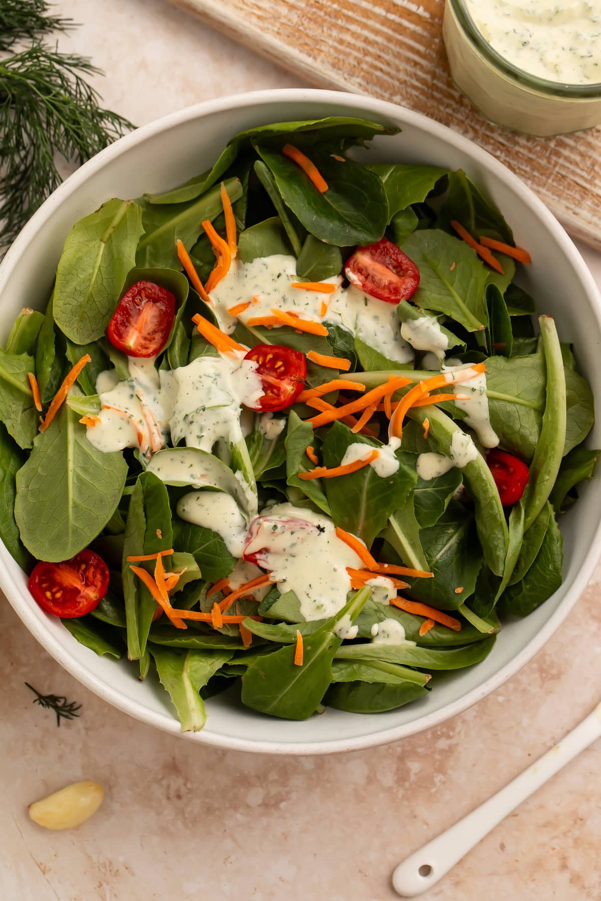 Overhead view of a green salad with cherry tomatoes, shredded carrots, and Whole30 ranch dressing