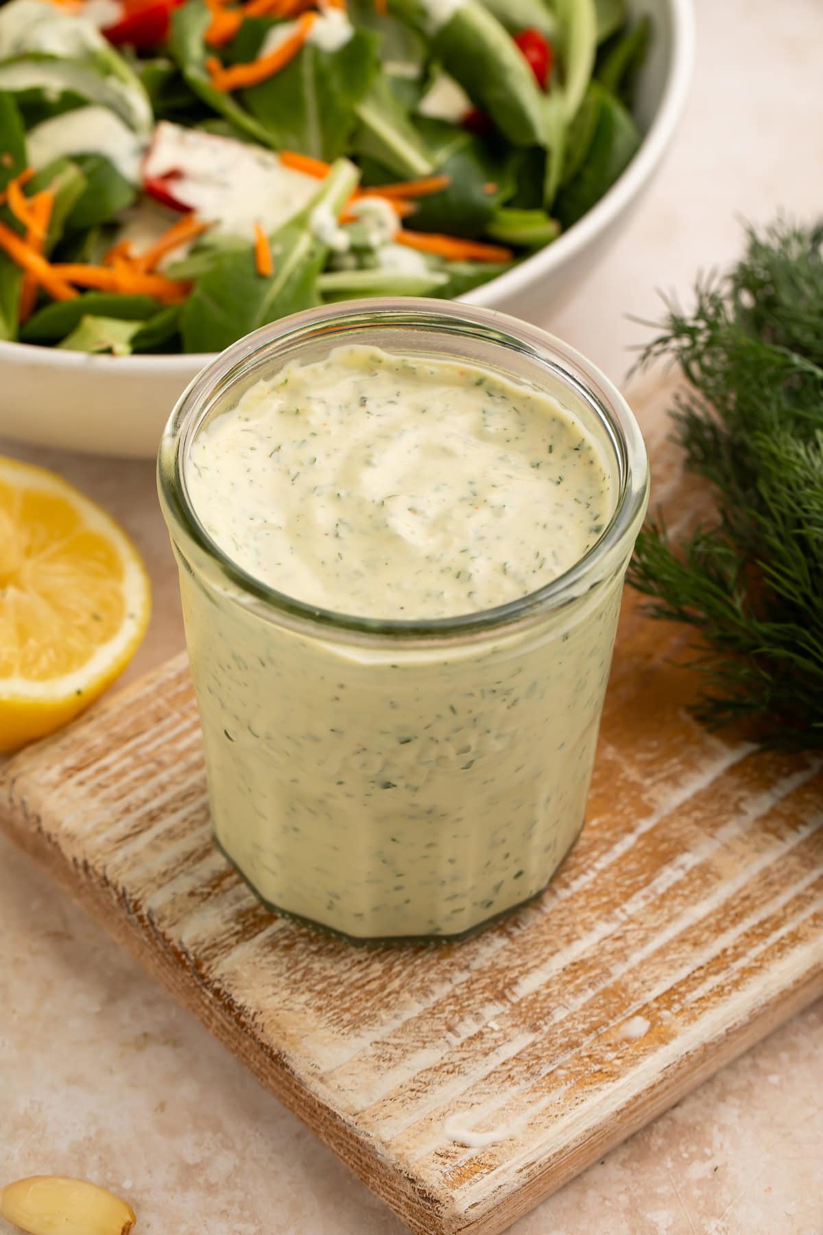 Glass jar of creamy herb ranch dressing on a wooden board with lemon and fresh dill