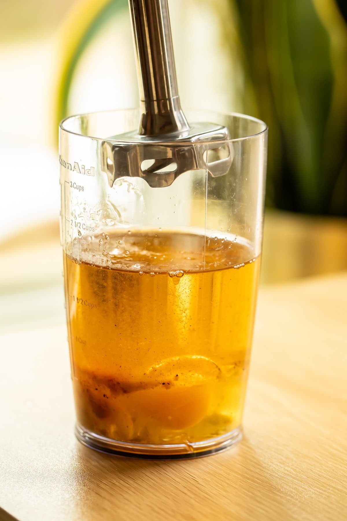 Immersion blender submerged in a clear jar filled with oil and eggs before blending